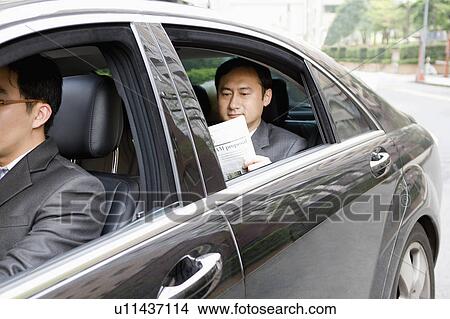 Picture - Man sitting in the car and reading newspaper. Fotosearch