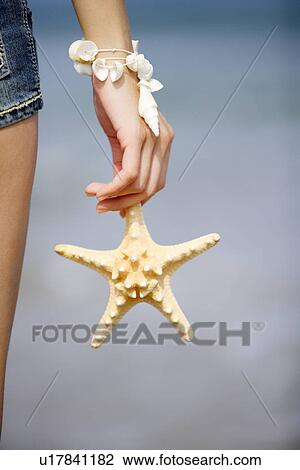 Stock Image - Woman holding one starfish, focus on hand. Fotosearch
