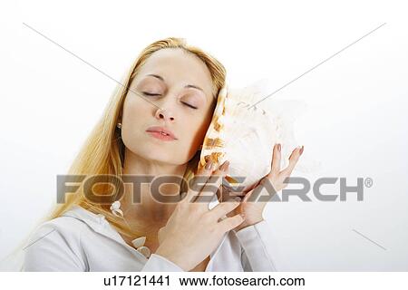 Young woman holding seashell to ear View Large Photo Image Stock Image - Young woman holding seashell to ear. Fotosearch