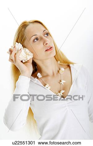 Stock Image - Young woman holding seashell to ear. Fotosearch