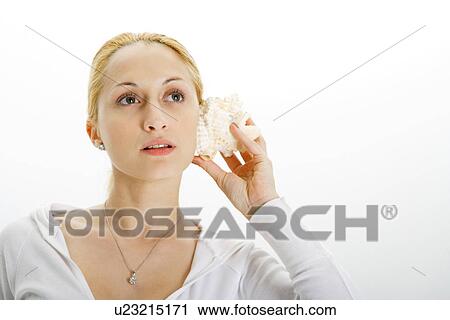 Stock Image - Young woman holding seashell to ear. Fotosearch