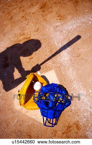 Stock Image - Baseball helmet, ball, glove and one person's shadow on base. Fotosearch