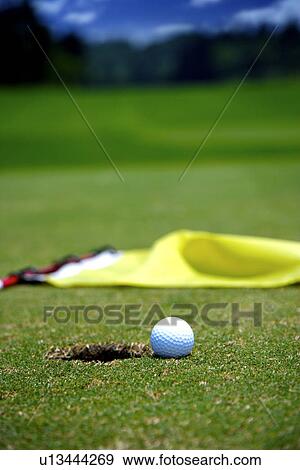 Golf ball at edge of hole, fallen flag View Large Photo Image Stock Photo - Golf ball at edge of hole, fallen flag. Fotosearch