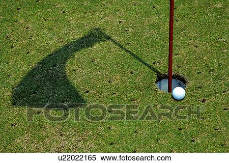Golf ball perched at edge of hole containing flag pole View Large Photo Image Stock Photography - Golf ball perched at edge of hole containing flag pole. Fotosearch