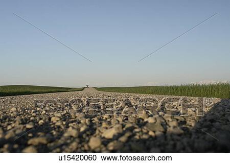 Stock Image - Extreme low angle of gravelled country road with oncoming vehicle; Canada, Manitoba, Erickson. Fotosearch