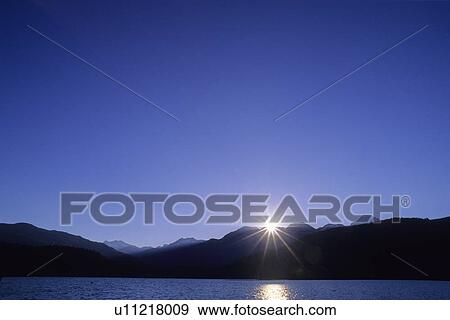 Sunburst over mountains at dawn, Green Lake at Whistler, BC View Large Photo Image Stock Photo - Sunburst over mountains at dawn, Green Lake at Whistler, BC. Fotosearch