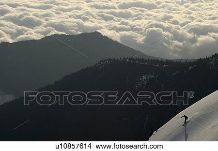 Picture - Silhouette of a skier above the clouds with mountain ridges in the background, Mount Arrowsmith, Port Alberni, BC. Fotosearch