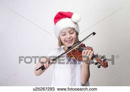 Stock Image - Girl - 6 years old playing violin in Santa hat. Fotosearch