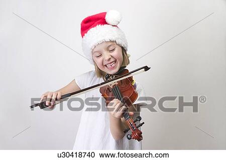 Stock Image - Girl - 6 years old playing violin in Santa hat. Fotosearch
