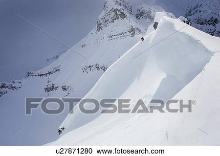 Stock Image - Skier on crest of big drop, dwarfed by mountain; Canada, British Columbia, Icefall Lodge. Fotosearch