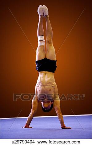 Young man practicing gymnastics on the floor, front view, headstand View Large Photo Image Picture - Young man practicing gymnastics on the floor, front view, headstand. Fotosearch