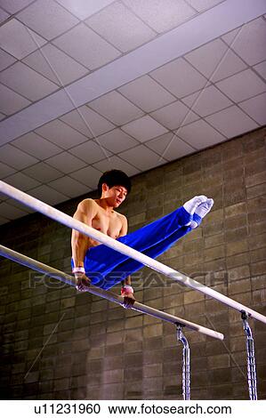 Stock Image - Young man practicing gymnastics on the parallel bars. Fotosearch