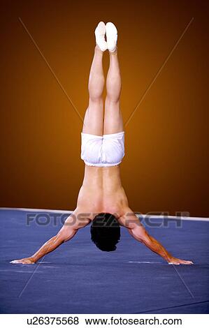 Stock Photo - Young man practicing gymnastics on the floor, rear view, headstand. Fotosearch