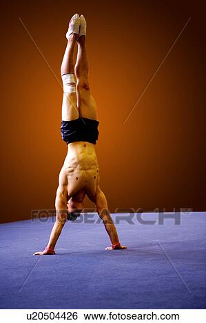 Stock Photograph - Young man practicing gymnastics on the floor, headstand. Fotosearch