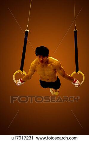 Stock Image - Young man practicing on the gymnastic rings, front view. Fotosearch