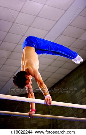 Picture - Young man practicing on the parallel bars, side view. Fotosearch