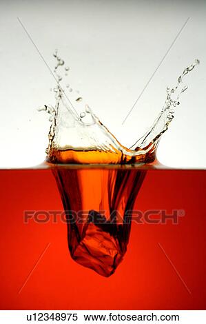 Stock Photography - Ice cube falling into the red water. Fotosearch