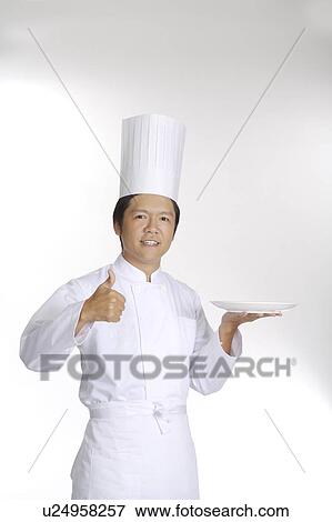 Stock Photo - Chef holding a plate and looking at the camera with thumbs up. Fotosearch