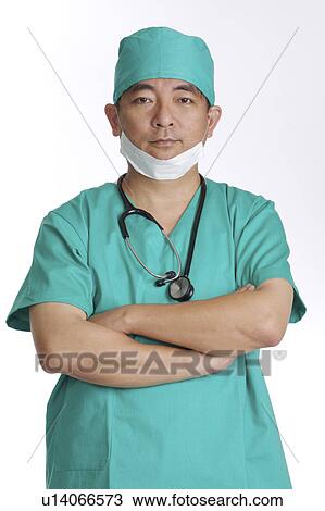 Stock Image - Doctor wearing operating gown and looking at the camera with hands on chest. Fotosearch