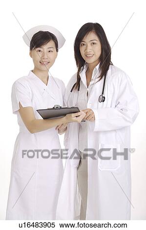 Stock Photography - Female doctor and nurse holding the clipboard and standing together. Fotosearch
