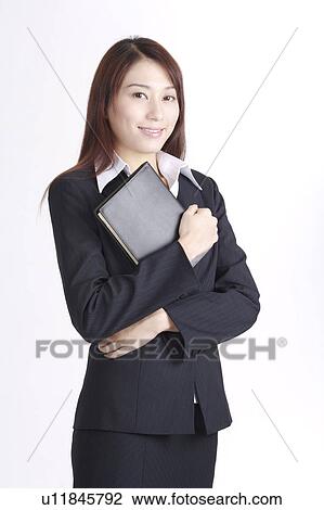 Stock Image - Young business woman holding a notebook and looking at the camera. Fotosearch