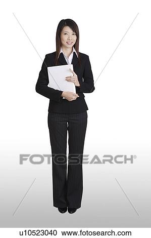 Stock Image - Young business woman standing and holding a laptop. Fotosearch