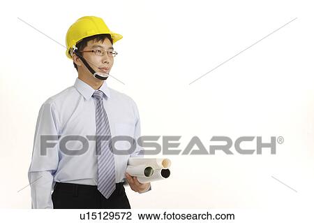 Stock Image - Young engineer wearing the helmet and holding the folded blueprint. Fotosearch