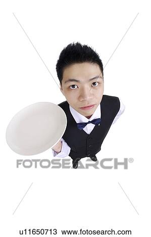 Stock Image - Young waiter holding a plate and looking at the camera. Fotosearch