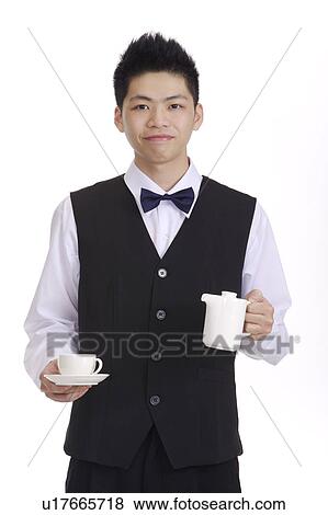 Young waiter holding a teapot, a cup and looking at the camera View Large Photo Image Stock Photo - Young waiter holding a teapot, a cup and looking at the camera. Fotosearch