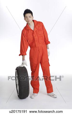 Stock Image - Young worker holding a tire and looking at the camera. Fotosearch