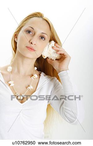 Young woman holding seashell to ear View Large Photo Image Stock Image - Young woman holding seashell to ear. Fotosearch