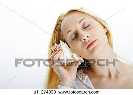 Young woman holding seashell to ear View Large Photo Image Stock Image - Young woman holding seashell to ear. Fotosearch