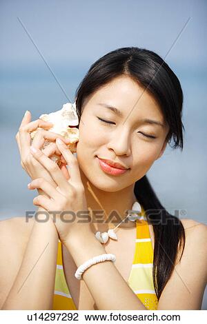Young woman holding seashell to ear View Large Photo Image Stock Image - Young woman holding seashell to ear. Fotosearch