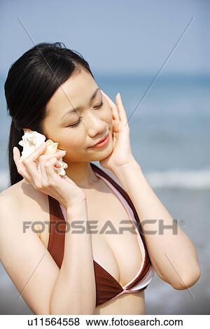 Young woman holding seashell to ear View Large Photo Image Stock Photo - Young woman holding seashell to ear. Fotosearch