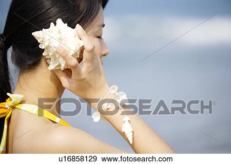 Young woman holding seashell to ear, side view View Large Photo Image Stock Photo - Young woman holding seashell to ear, side view. Fotosearch
