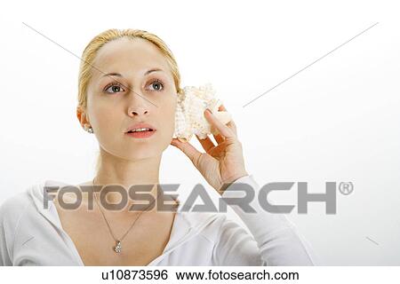 Stock Photograph - Young woman holding seashell to ear. Fotosearch
