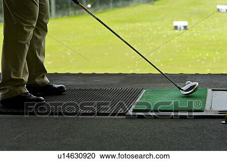 Stock Image - A man hitting golf balls at a driving range. Fotosearch