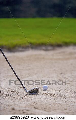 Stock Image - Close-up of a golf club and a golf ball in sand trap. Fotosearch