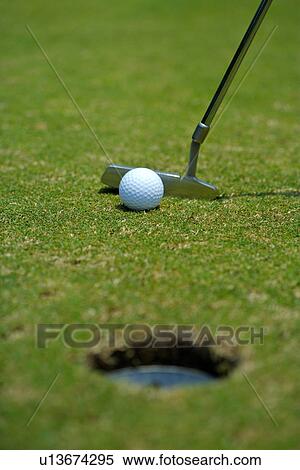 Stock Photography - Golf ball and putter beside hole, close up. Fotosearch