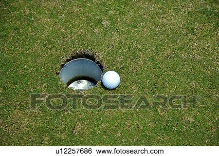 Stock Photograph - Golf ball perched at edge of hole. Fotosearch