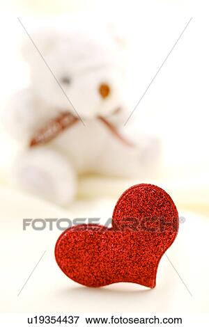 Stock Photo - Heart shaped object, teddy bear in the background. Fotosearch