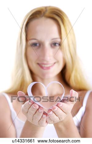 Stock Image - Young woman holding heart shape, smiling, portrait. Fotosearch