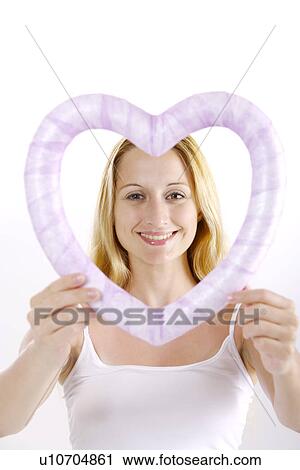Stock Image - Young woman holding heart shaped object. Fotosearch