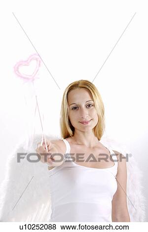 Stock Photo - Young woman wearing angel wings holding magic wand, smiling, portrait. Fotosearch