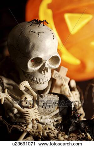 Stock Image - Human skeletons and illuminated pumpkin. Fotosearch