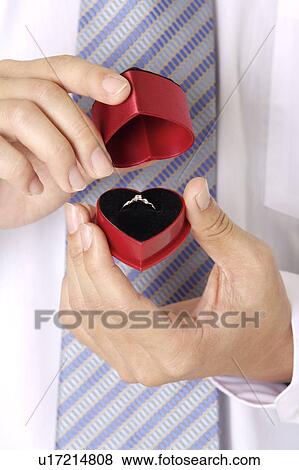 Stock Photo - Man holding a heart shape jewelry box with diamond ring inside. Fotosearch