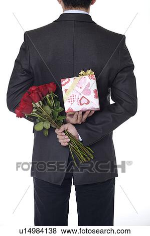 Man holding a wrapped gift and roses behind back View Large Photo Image Stock Photo - Man holding a wrapped gift and roses behind back. Fotosearch