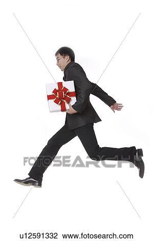 Stock Image - Man holding a wrapped gift and running, side view. Fotosearch
