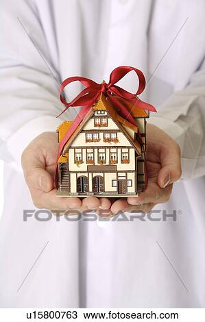 Stock Image - Man's hands holding a house model as a gift. Fotosearch