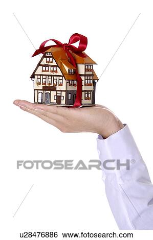 Stock Photograph - One hand holding a house model with red bowknot. Fotosearch